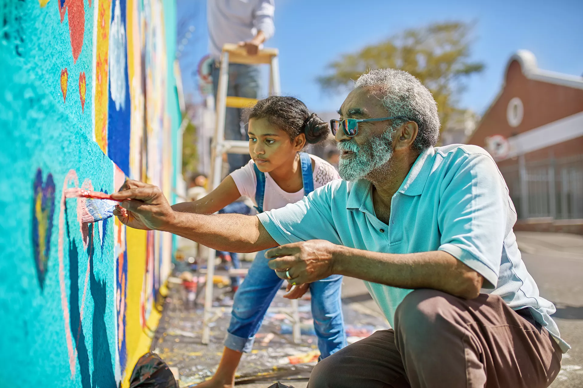 Older man and child painting a mural on a school yard wall